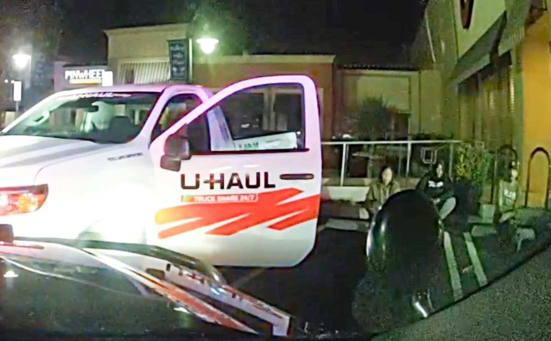 3 people sitting on a curb next to a U-Haul truck
